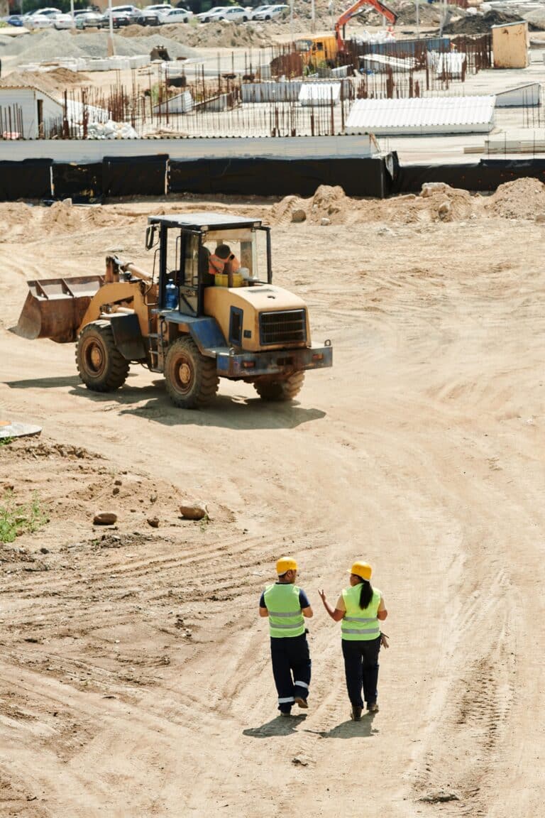 Wheel loader and two workers in high-visibility vests on a civil construction earthworks site