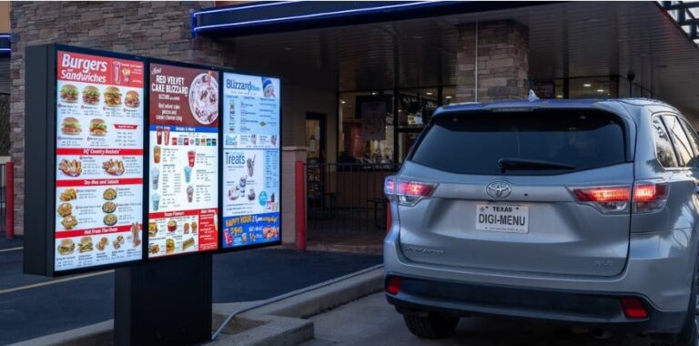 Digital drive-thru menu boards lit at dusk with a car waiting at the order point
